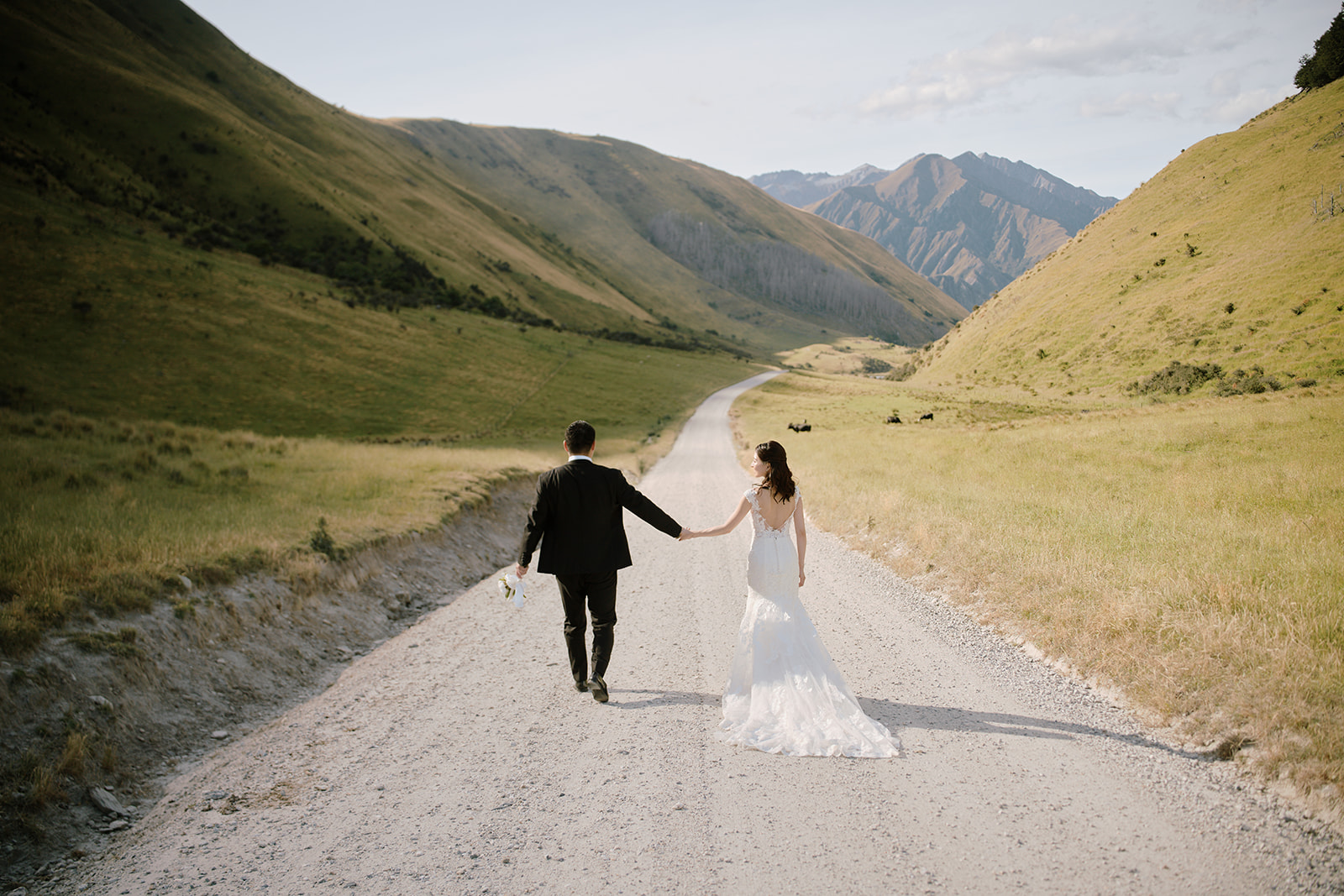 Queenstown Wedding Photographer A bride and groom walking down a dirt road in ウェディングプランニュージーランド the mountains.